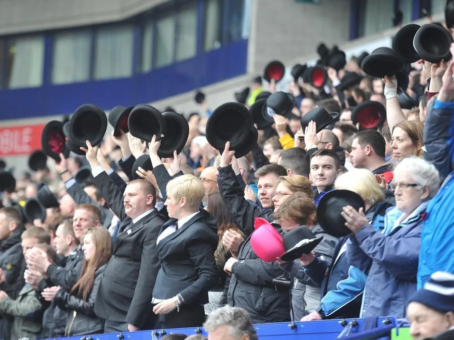 Older crowd scene with supporters holding up bowlers in the stand.